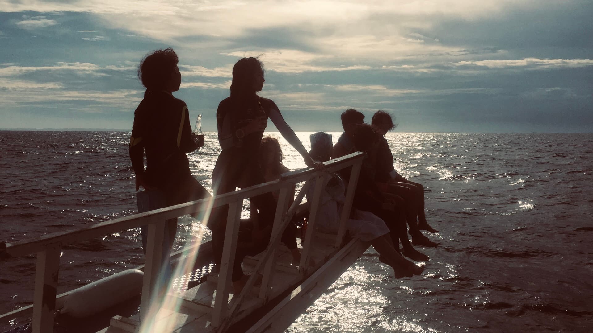 Divers in wetsuits resting on a boat ladder, backlit over the sea