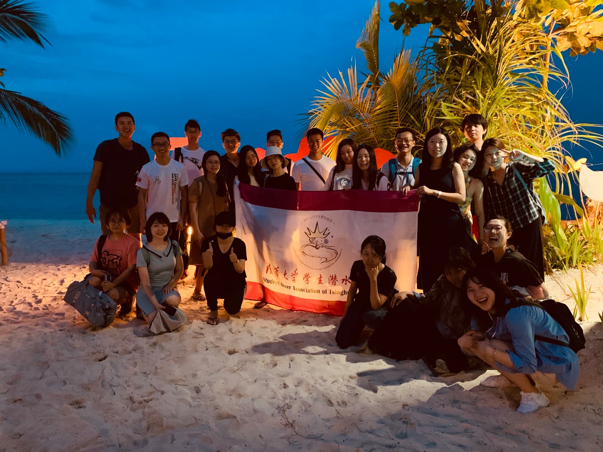 Tsinghua student diver association posing with their banner on a beach at dusk
