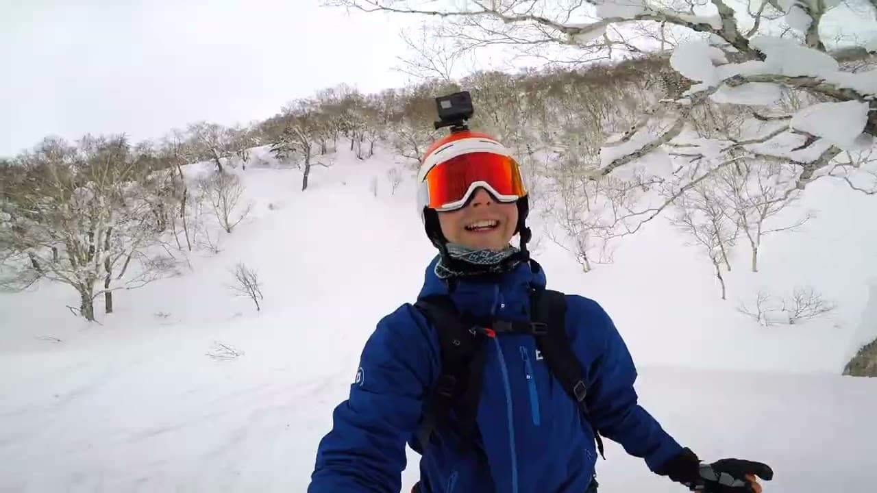 Still from the Niseko trip video: a smiling snowboarder in goggles and a GoPro helmet on a powder slope