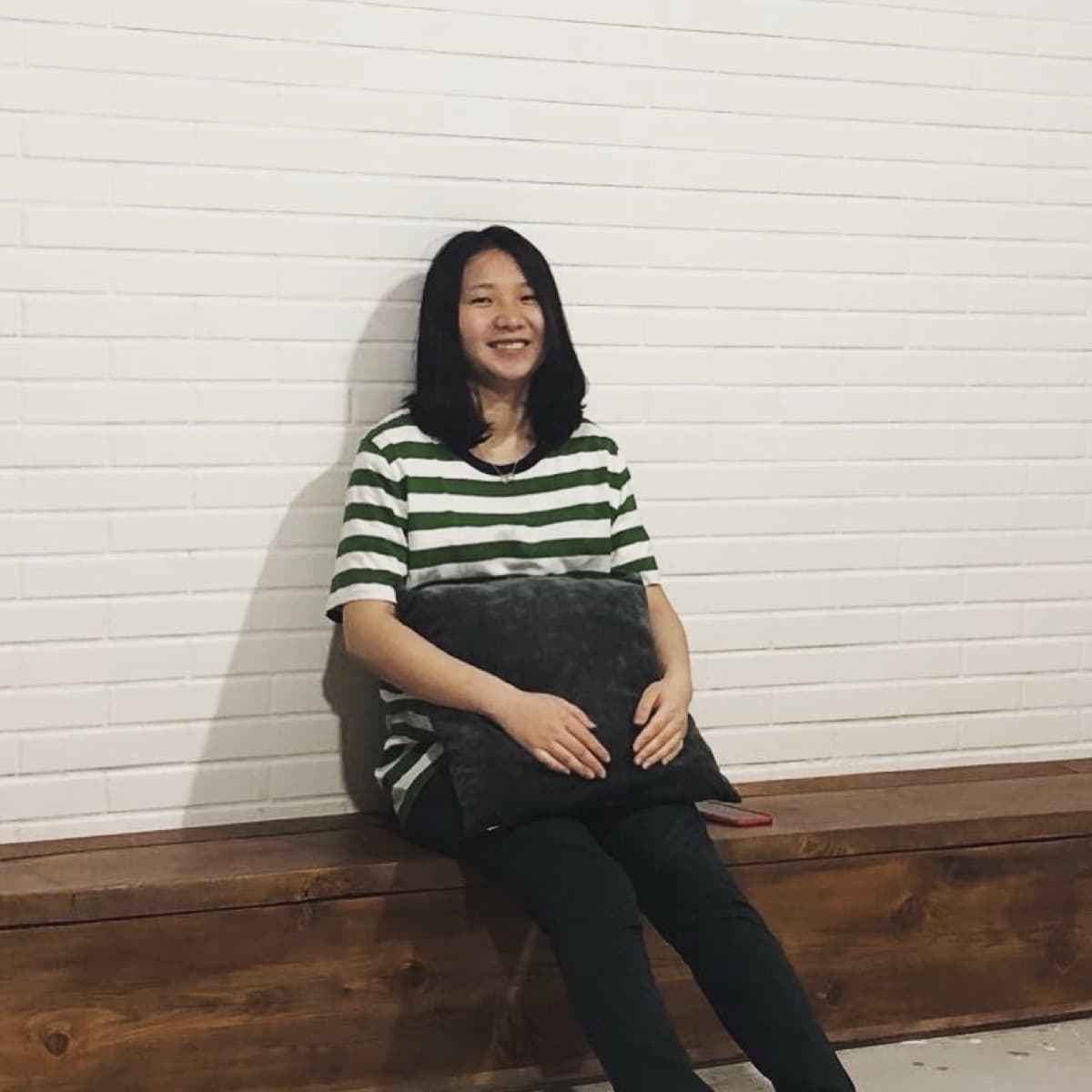 Sherry sitting on a wooden bench in a green striped shirt, smiling